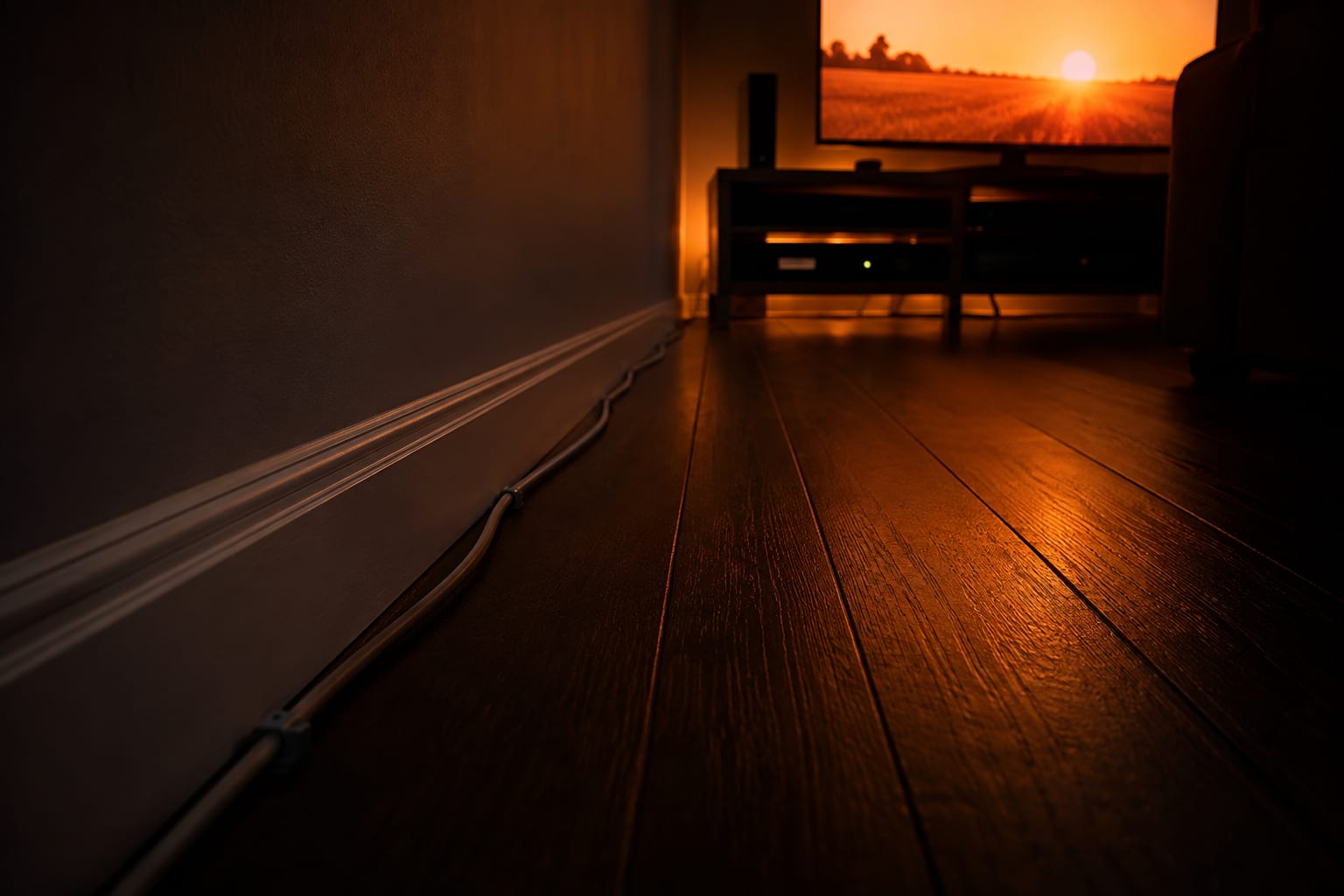 Ethernet cable running along a skirting board across a dark floor toward a television stand