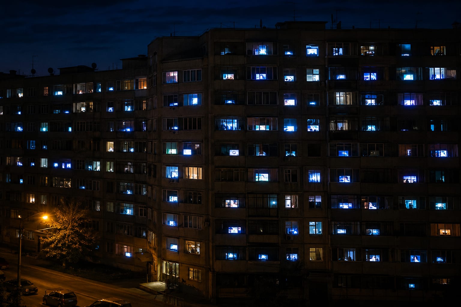 Apartment building at night with many windows glowing from television screens